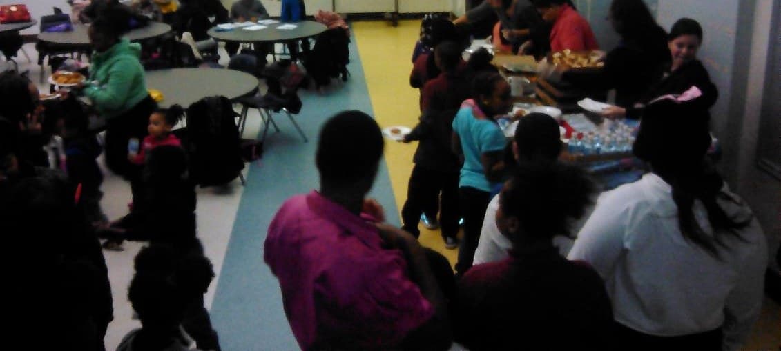 Families gathering in a school cafeteria while dinner is served
