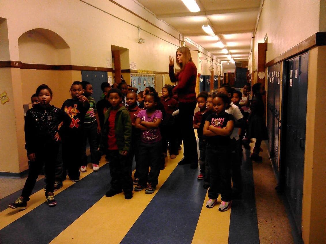 A class of students waiting in a school hallway with their teacher