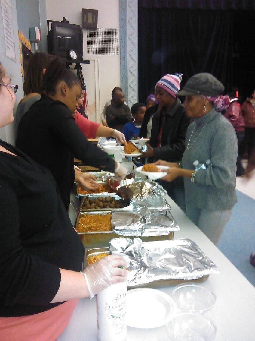 Families being served dinner along a buffet line in a school hall