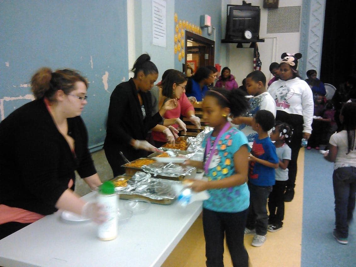 Volunteers serving dinner to students at an A+ Plus Detroit family social