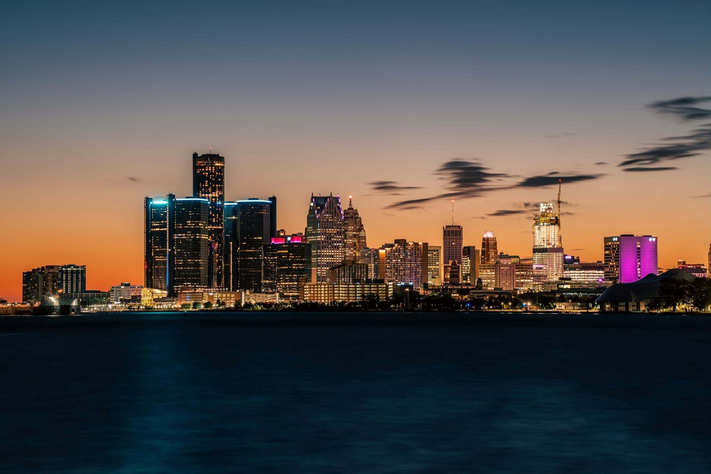 Downtown Detroit skyline lit up at dusk, seen from across the Detroit River
