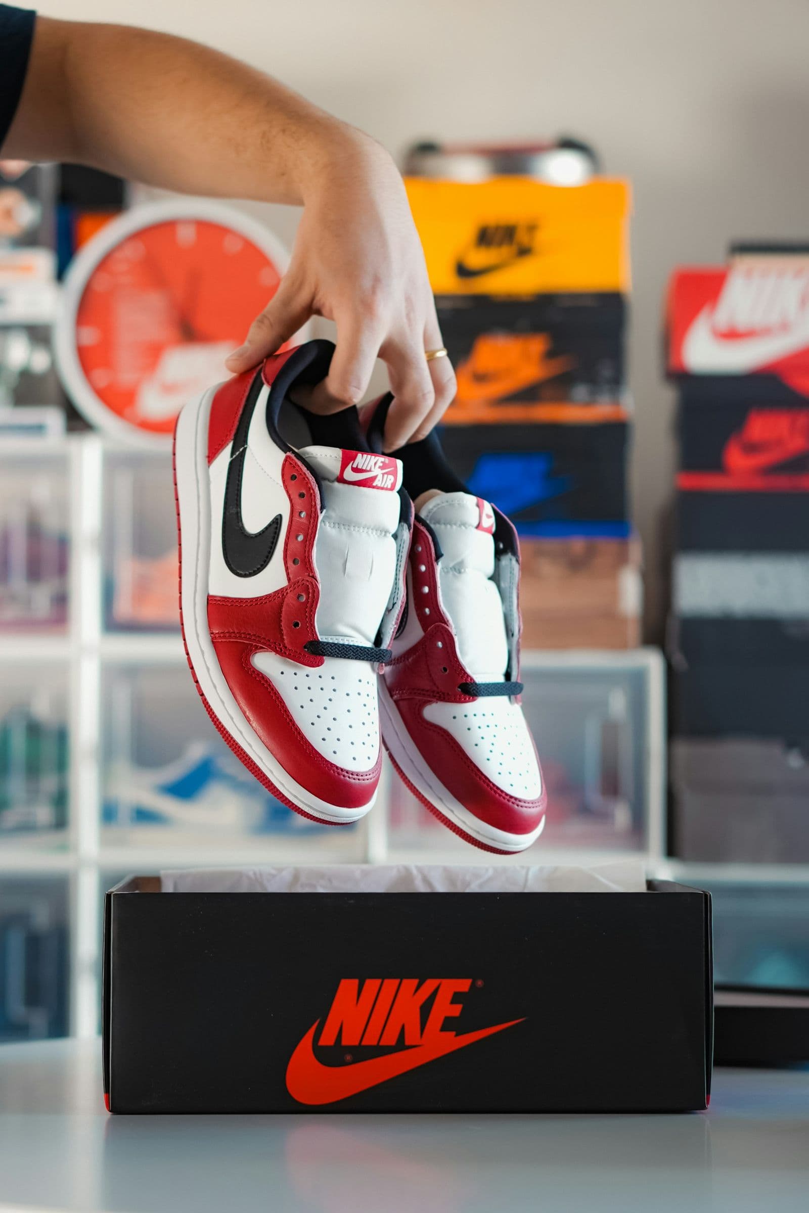 Hand holding up a pair of red and white Air Jordan 1 Lows over a Nike box